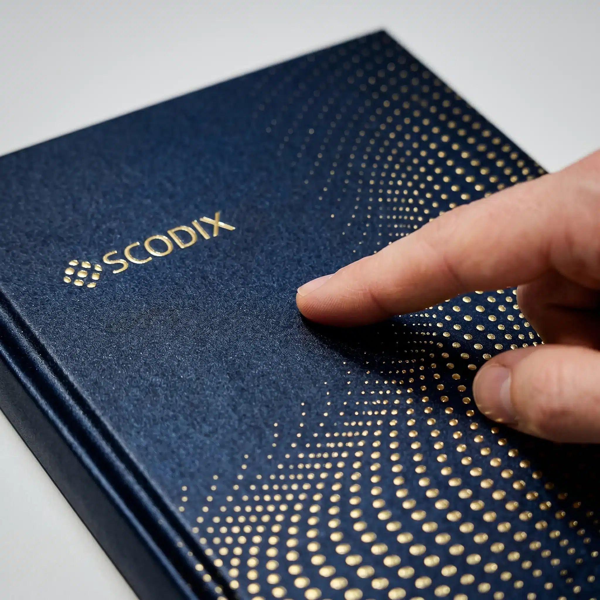 Tactile print finishing, New York City, blue paper with gold foil dots Tactile print finishing in New York City shows blue material with gold dot pattern and a fingertip checking raised texture details.