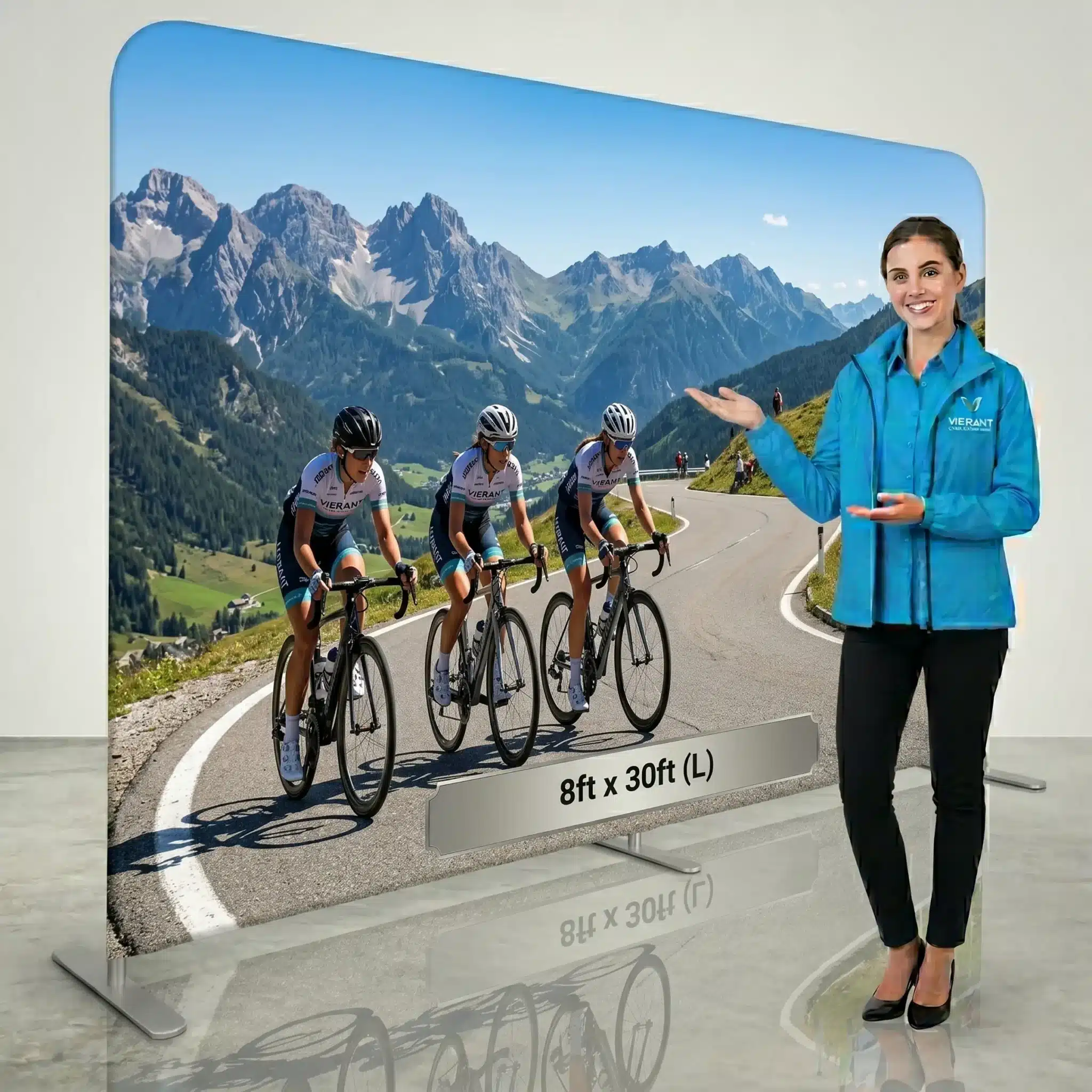 Mountain road cycling display stand, Swift pillowcase fabric backdrop with presenter A large Swift pillowcase fabric display stand shows cyclists climbing a mountain road while a presenter in a blue jacket stands beside it.